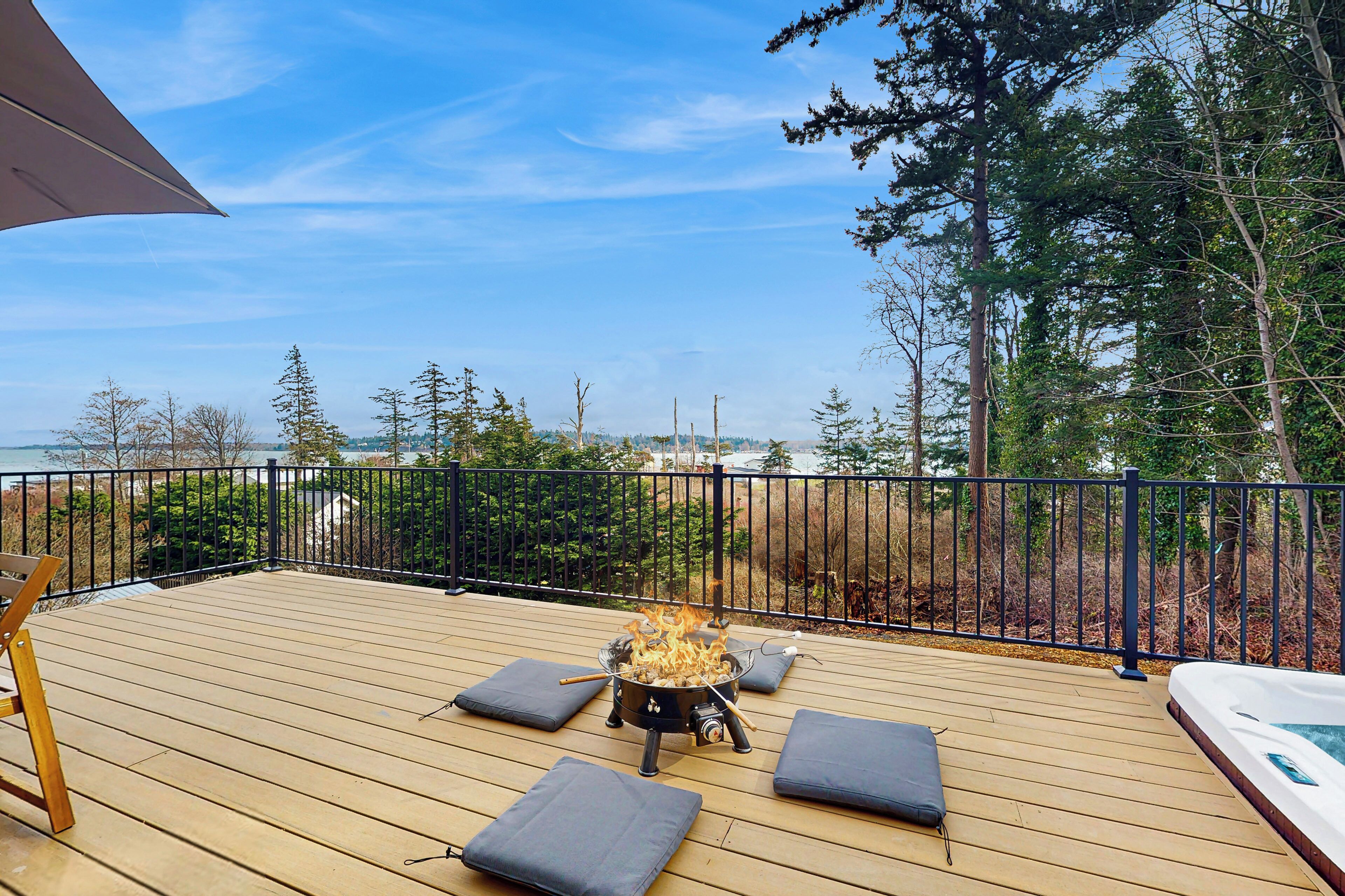 A wooden deck with a fire pit, outdoor seating, and a view of the ocean.