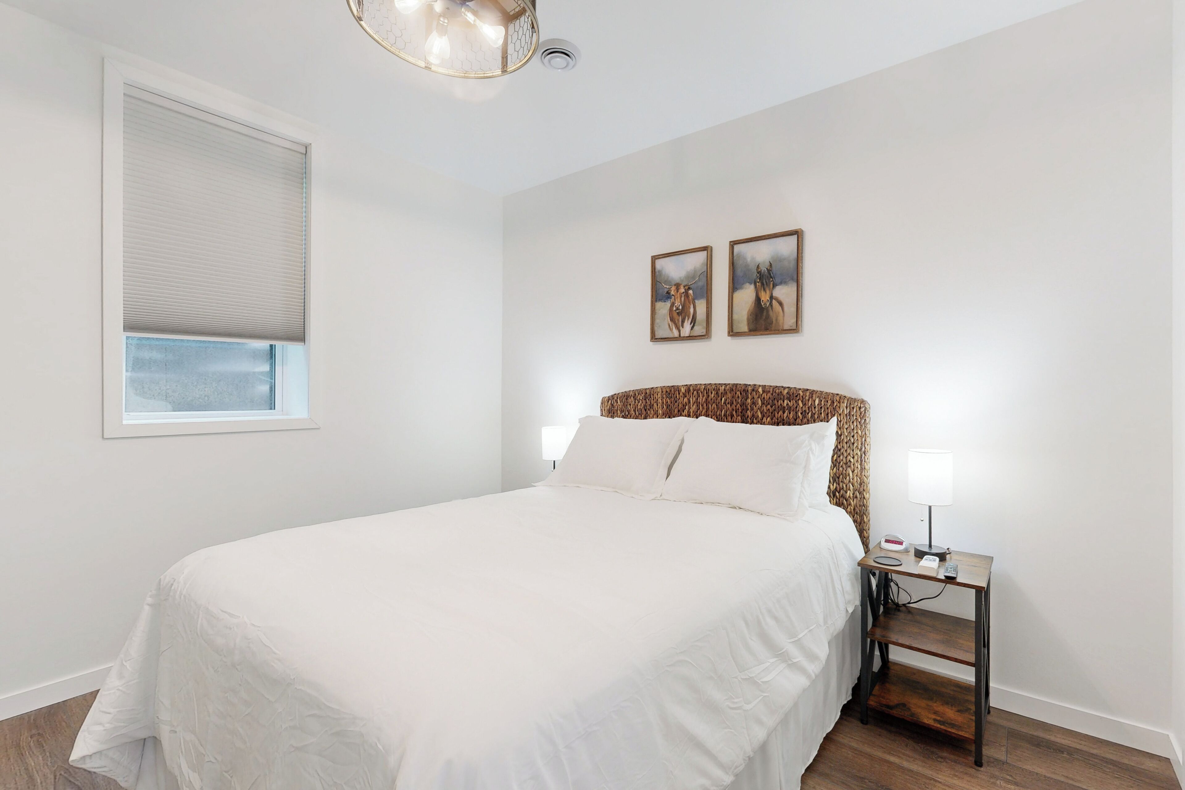 A bedroom with a large bed, a bedside table with a lamp, and two framed pictures on the wall.