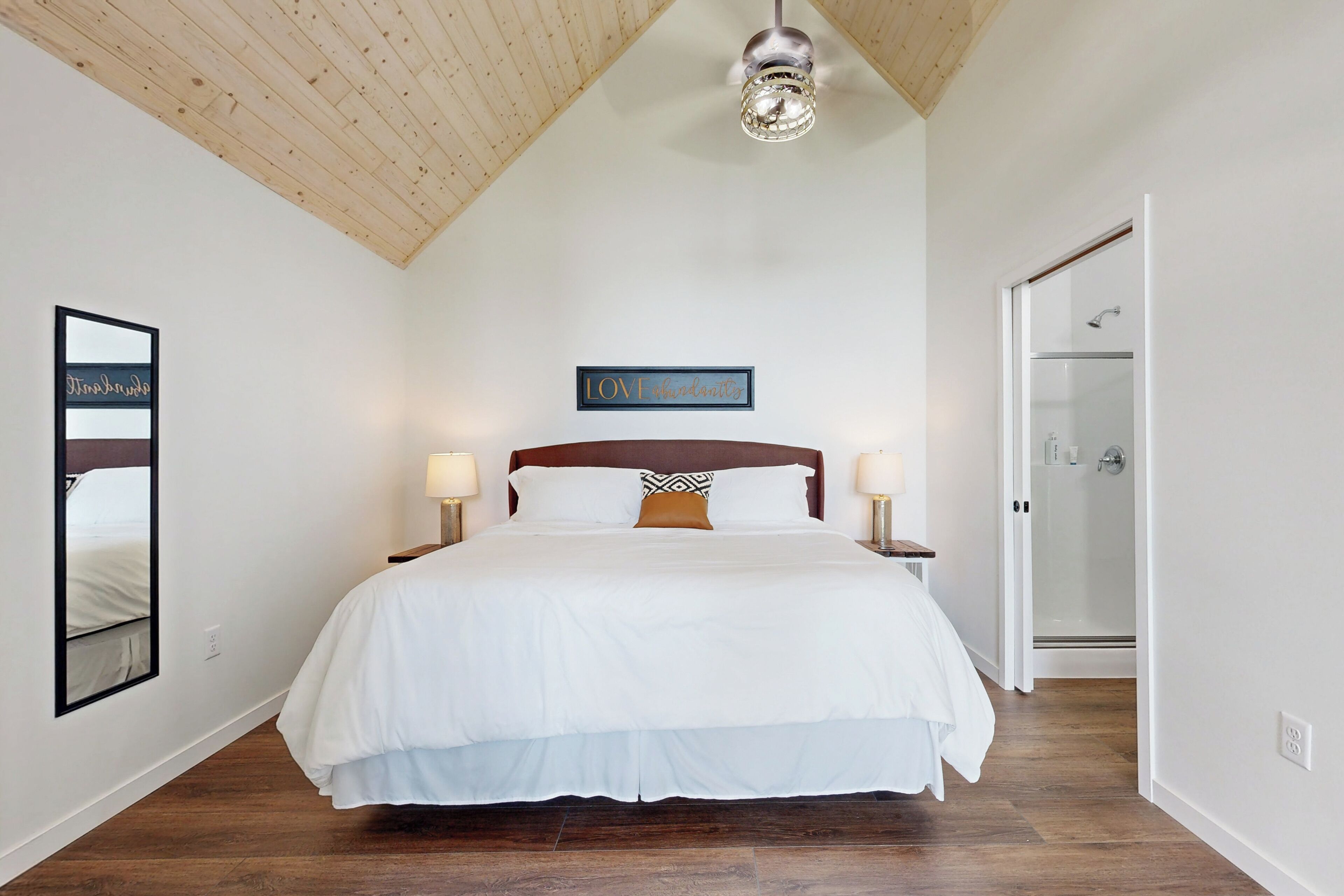 A bedroom with a large bed, wooden ceiling, and a glass shower door.