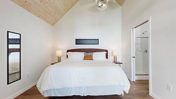 A bedroom with a large bed, wooden ceiling, and a glass shower door.