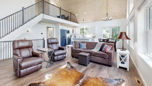 A spacious living area with leather recliners, a brown leather sofa, and a large leather rug. A staircase leads to an upper level.