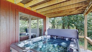 A hot tub under a wooden pergola with a glass door leading to a patio area.
