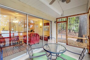 Un intérieur chaleureux avec une porte vitrée donnant sur une zone boisée, une table ronde en verre et un canapé rouge.