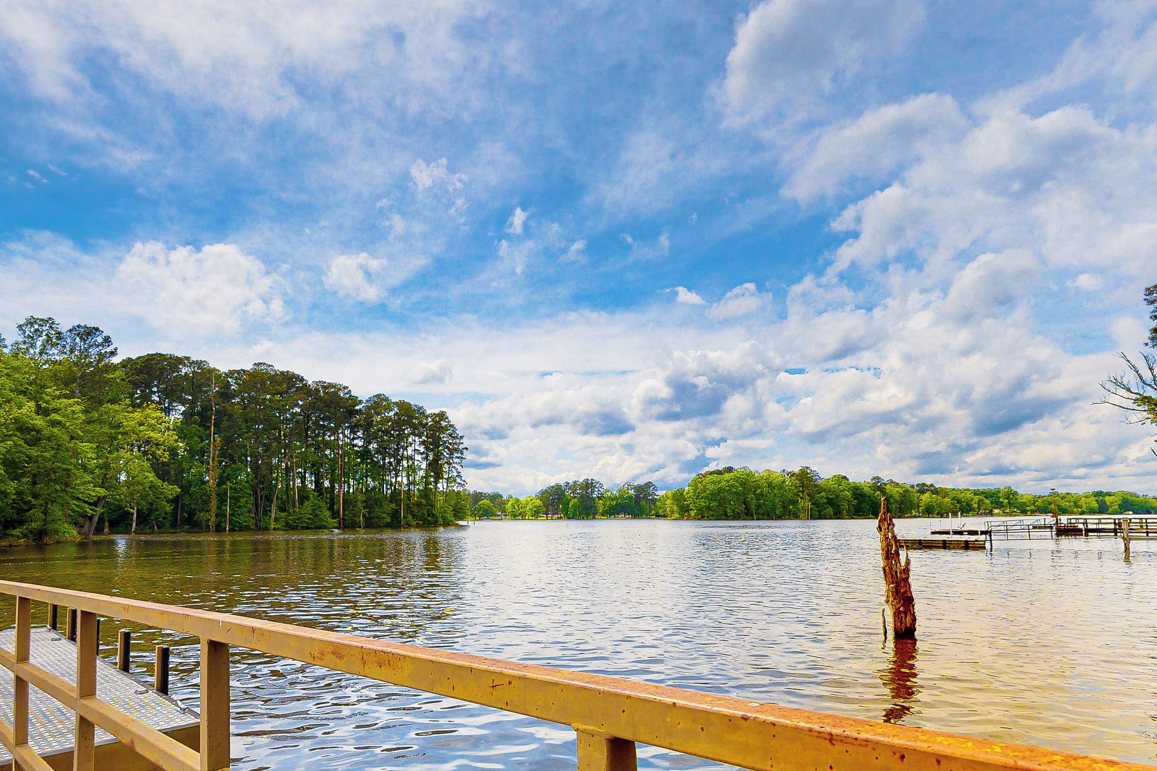 A wooden dock extending into a calm lake with a forested shoreline and a cloudy sky.
