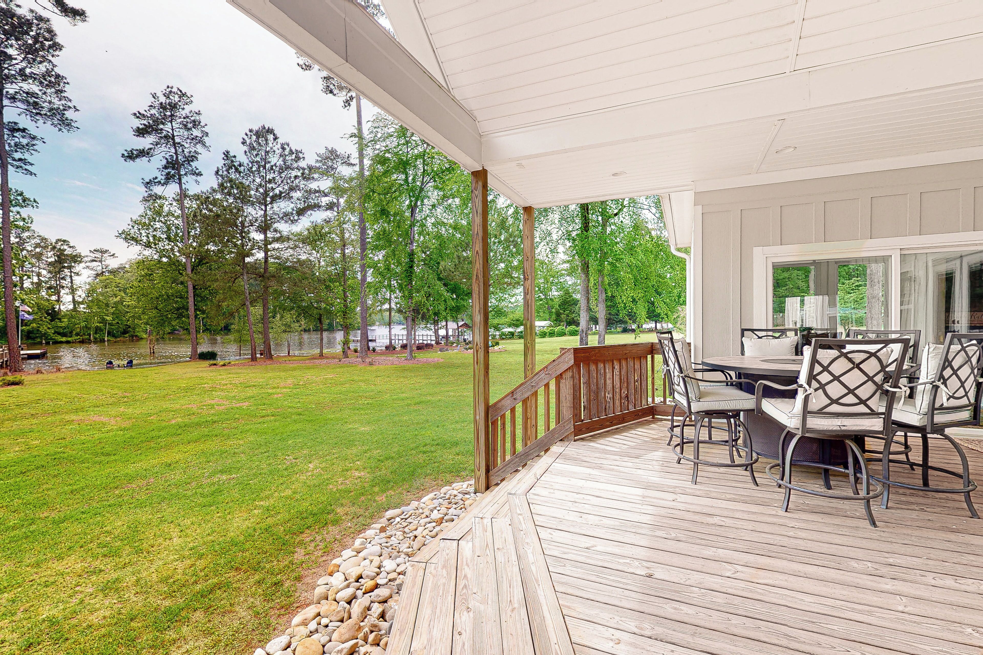 A covered patio with a dining table and chairs, surrounded by a wooden deck and a stone border.
