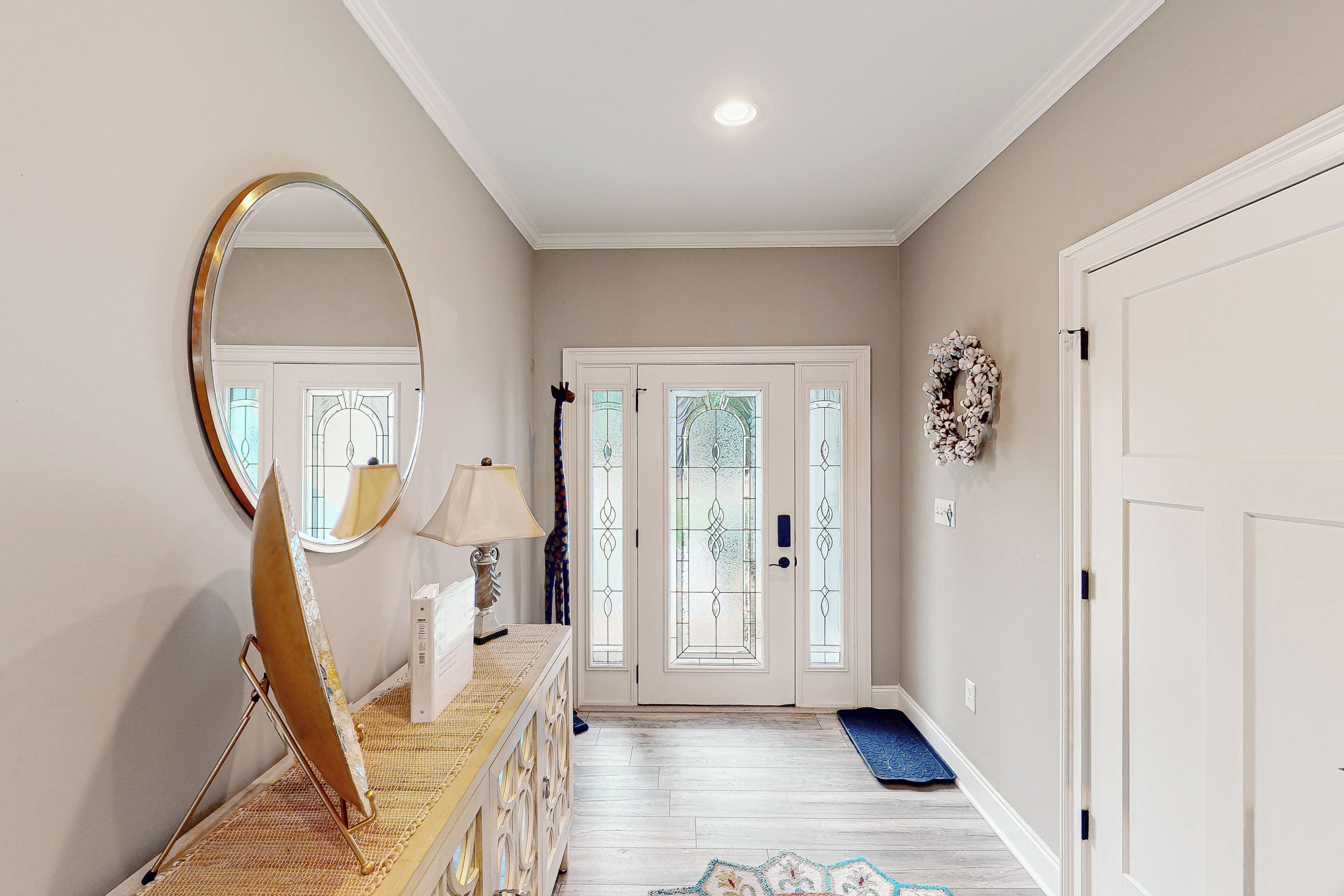 A hallway with a mirror, a lamp, a decorative mirror frame, a mat, and a door with glass panels.