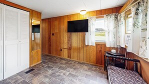 A room with wooden walls, a television mounted on the wall, a bench, and a window with curtains. - Countryside Couples Retreat! Gateway to Corning (Cameron Mills)