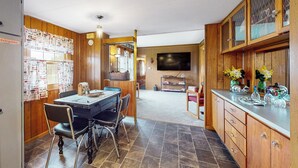 A kitchen with wooden cabinets, a dining table with chairs, a television, and a kitchen island. - Countryside Couples Retreat! Gateway to Corning (Cameron Mills)