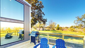 Una terraza con dos sillas Adirondack azules, una parrilla y vistas a un área verde con árboles.