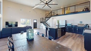 Una cocina amplia con una isla central, un comedor con una mesa de madera y una sala de estar con un televisor grande y asientos.