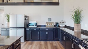 A modern kitchen with dark cabinetry, a stainless steel refrigerator, a microwave, and a coffee maker. There are two potted plants on either side of the counter. - Lakefront Oasis w/ Water Toys! Breckenridge Home (Breckenridge)