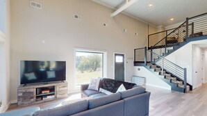 A spacious living room with a large flat-screen TV, a grey sofa, and a staircase leading to an upper level. - Lakefront Oasis w/ Water Toys! Breckenridge Home (Breckenridge)