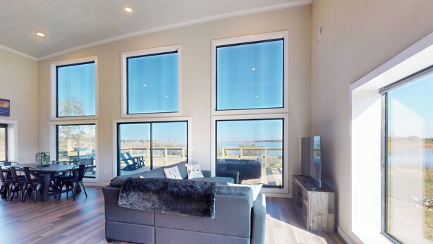 A spacious living area with large windows, a grey sofa, a dining table with chairs, and a flat-screen TV. - Lakefront Oasis w/ Water Toys! Breckenridge Home (Breckenridge)