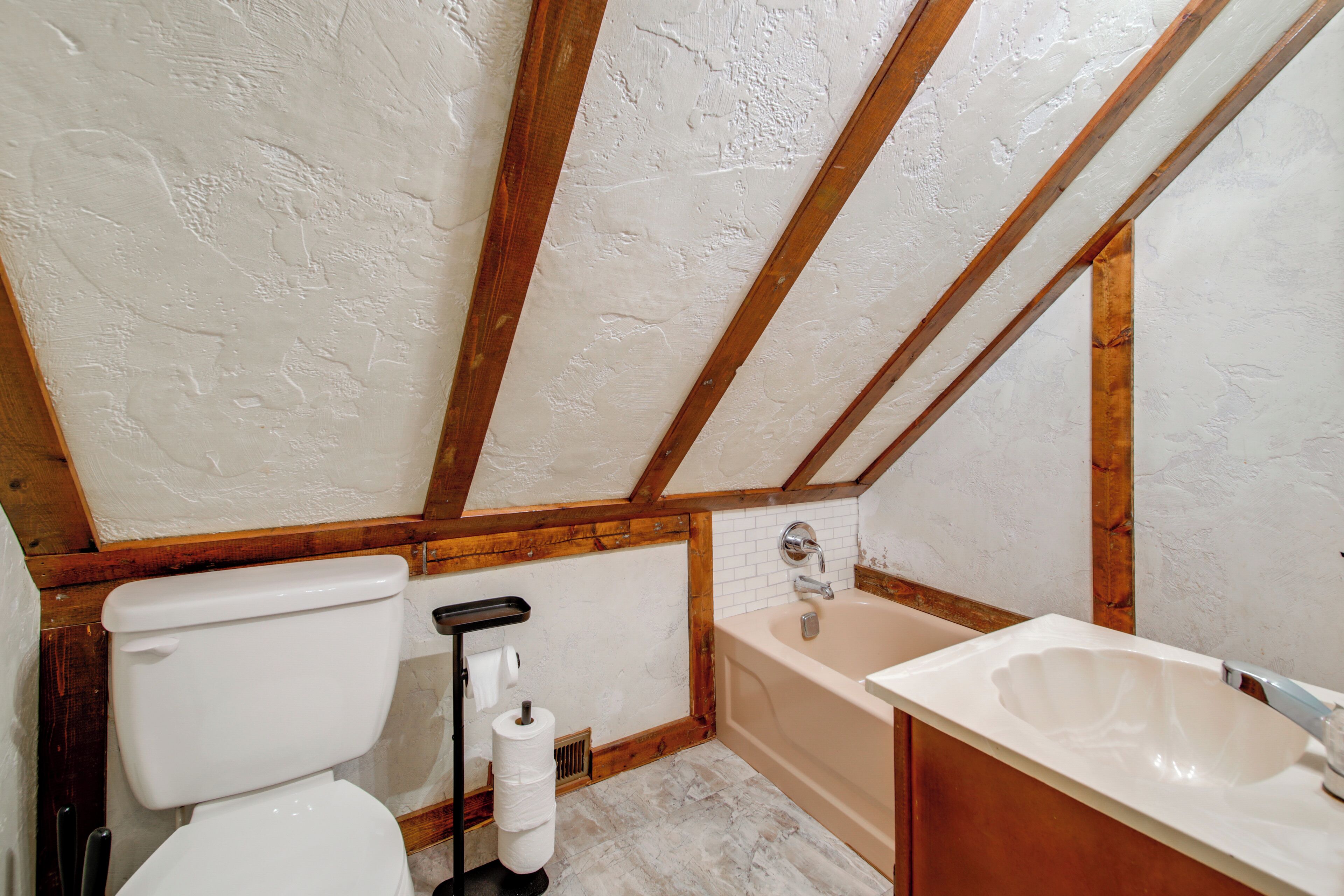 Une salle de bain avec des toilettes, un lavabo et une baignoire, des poutres en bois au plafond et des murs blancs.