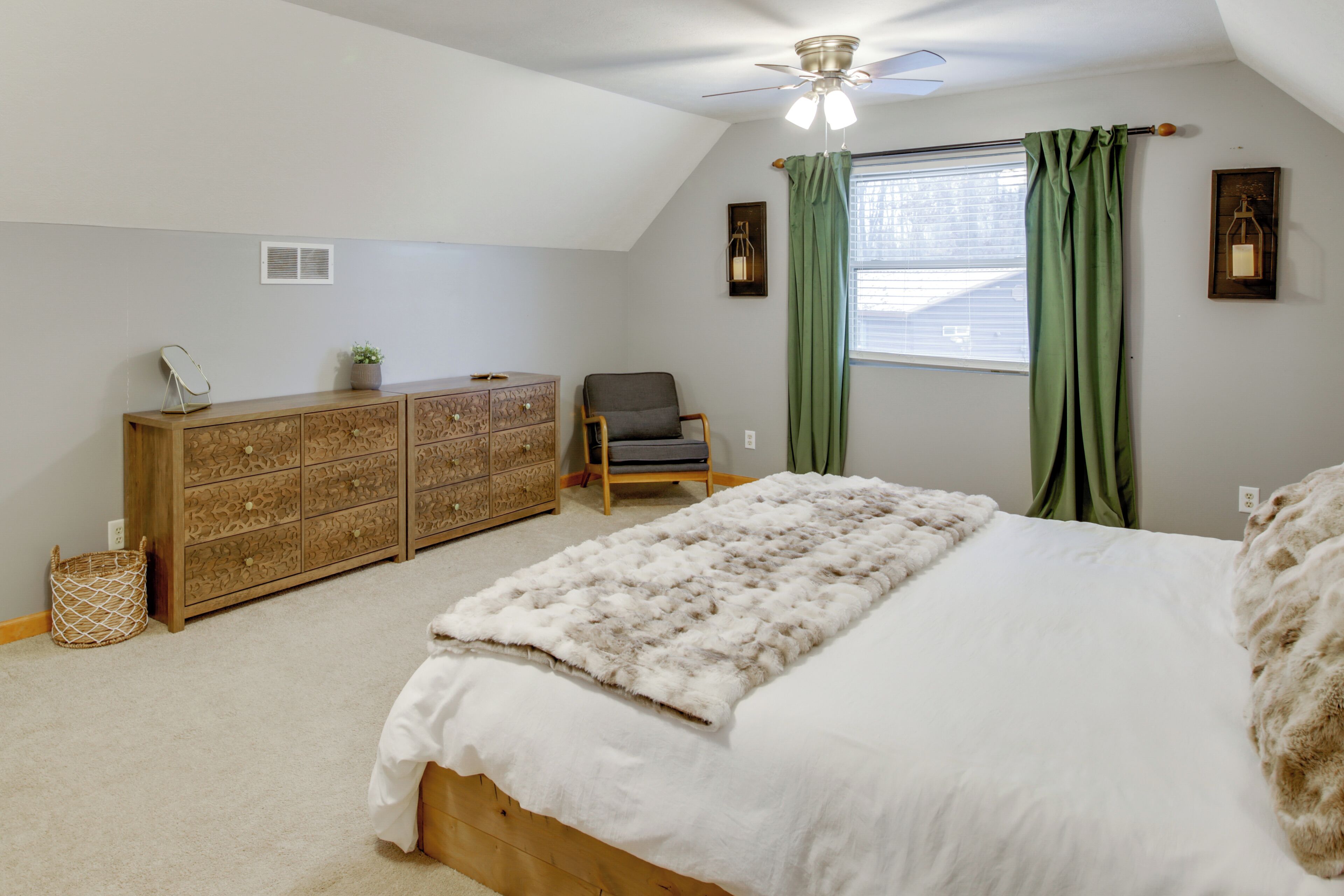A bedroom with a bed, a dresser, a chair, a window with curtains, and a ceiling fan.