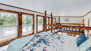A bedroom with a large bed, wooden beams, and a view of trees through the windows. - River-view Home w/ Fire Pit & Grill! (Cedar Bluff)