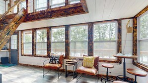 A spacious room with large windows, a wooden staircase, and a cozy seating area with leather chairs and a small table. - River-view Home w/ Fire Pit & Grill! (Cedar Bluff)