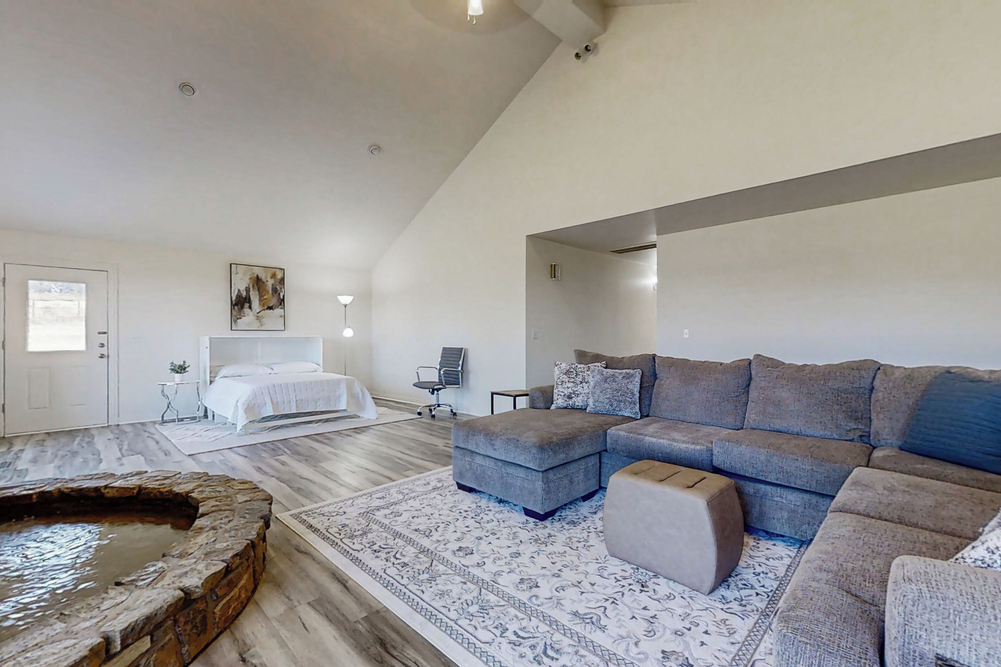 Una sala de estar amplia con un sofá seccional gris grande, una chimenea de piedra y una cama en la habitación contigua.