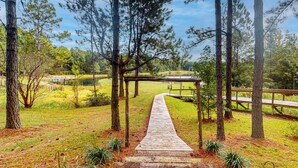 A wooden pathway leading through a forested area with a wooden bridge over a body of water. - Serene 3BR Farmhouse w/ Deck & Pond (Wilmer)