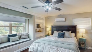 A bedroom with a bed, window seat, ceiling fan, bedside lamps, and a wall-mounted air conditioner. - Serene 3BR Farmhouse w/ Deck & Pond (Wilmer)