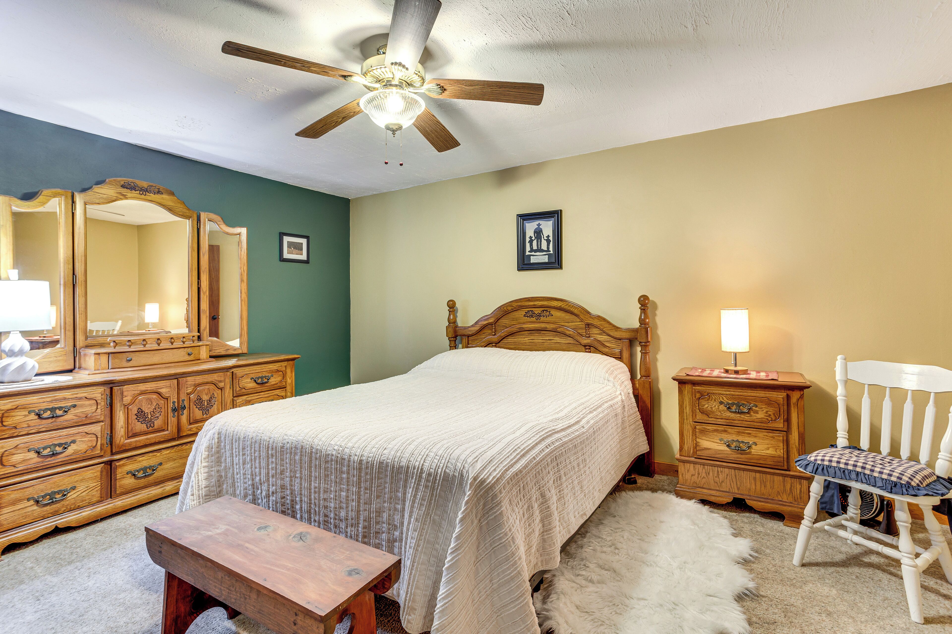 A bedroom with a bed, wooden dresser, chair, and a ceiling fan.