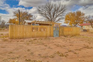 Une zone délimitée par une clôture, avec une structure en bois, possiblement un abri ou un petit bâtiment, dans un environnement désertique caractérisé par une végétation clairsemée et des arbres sans feuilles.
