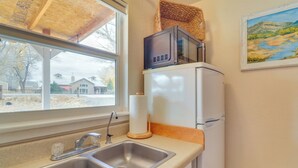Une cuisine équipée d’un évier à deux bacs, d’un four à micro-ondes posé sur un réfrigérateur blanc, et d’une fenêtre donnant sur des maisons.