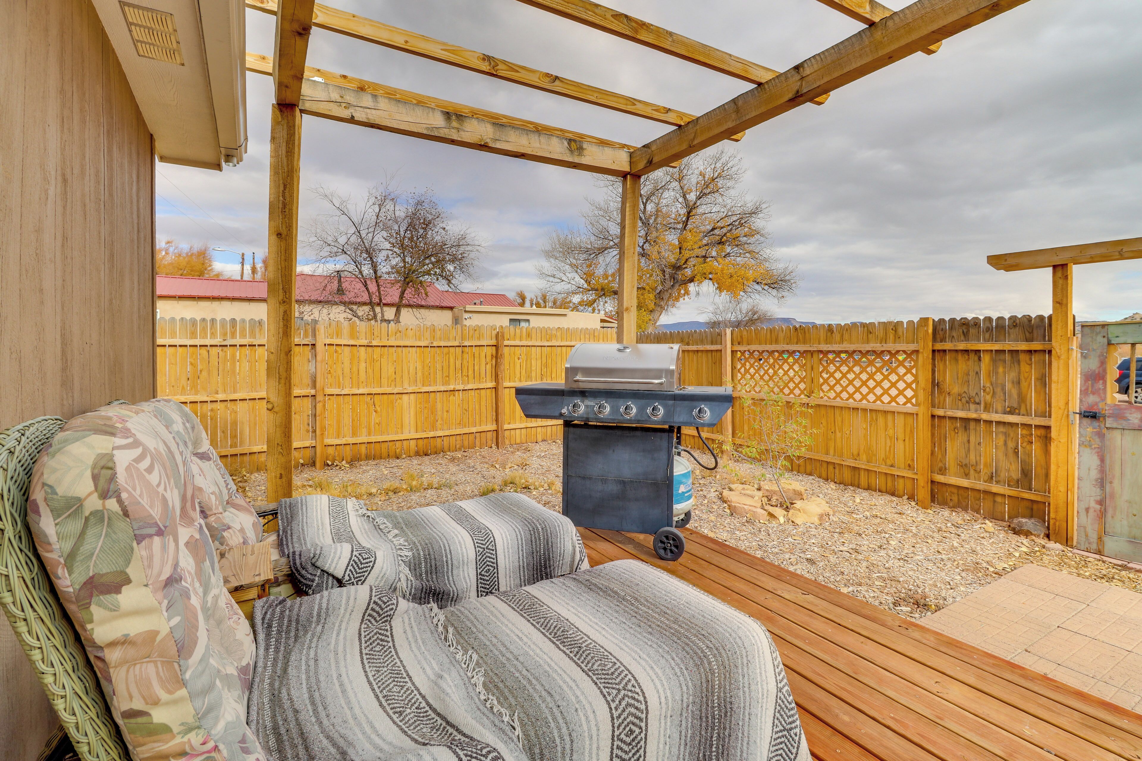 A covered outdoor seating area with a wooden deck, a grill, and a view of a fenced backyard.