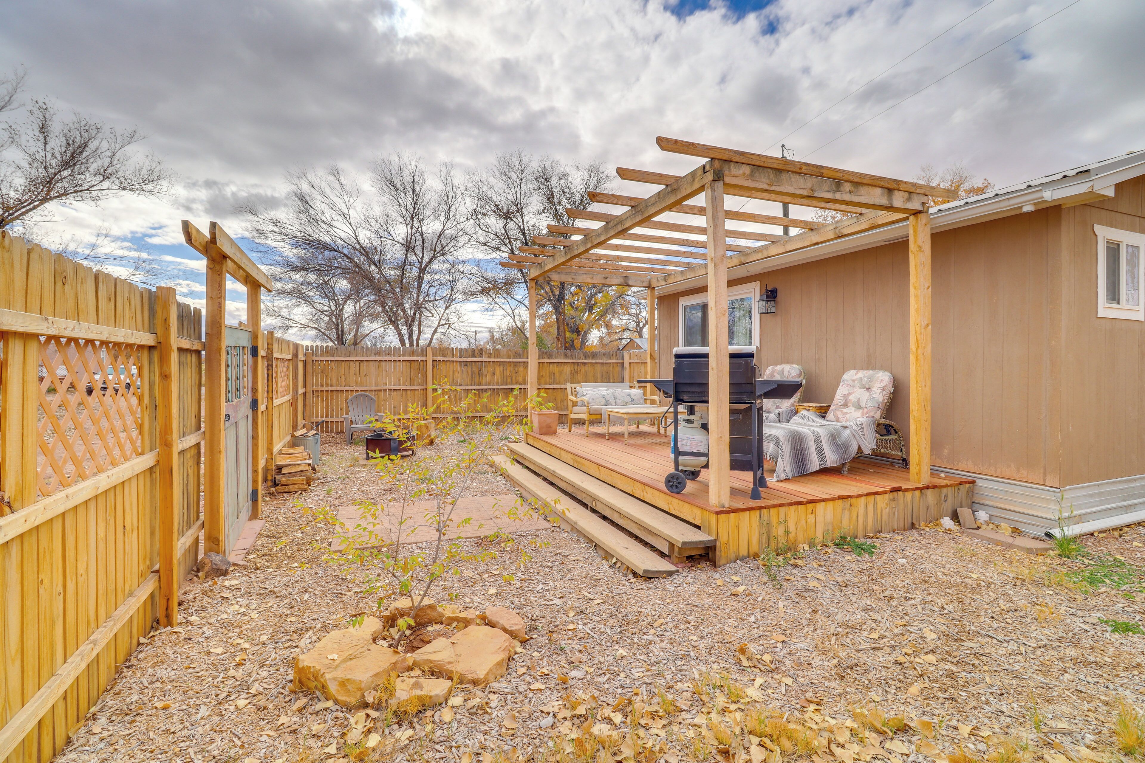 Ein Hinterhof mit einer Holzterrasse, einem Grill, Sitzgelegenheiten im Freien und einer Pergola.