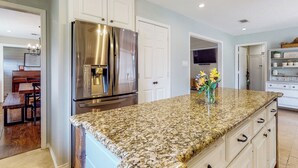 A kitchen with white cabinets, a stainless steel refrigerator, a granite countertop, and a vase with flowers. - Pool, Hot Tub & Pool Table! Grand Home in Tomball (Tomball)
