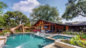 A pool area with a slide, lounge chairs, and a wooden building with a patio. - Pool, Hot Tub & Pool Table! Grand Home in Tomball (Tomball)