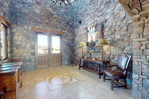 Quarto com paredes de pedra, uma escrivaninha de madeira, uma cadeira e um abajur.