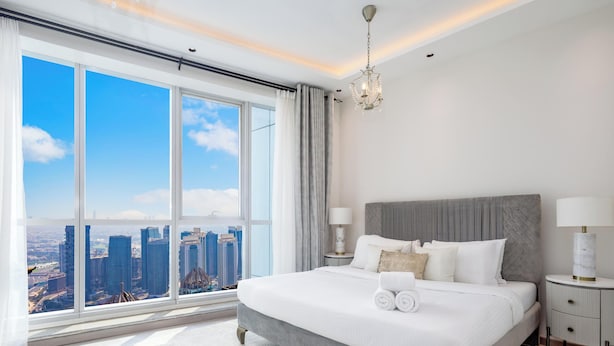 Ein modernes Hotelzimmer mit großem Fenster und Blick auf die Stadt, einem ordentlich bezogenen Bett und einer Kristallleuchter.