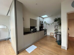 A modern kitchen with a microwave, stove, and sink. There is a small wooden stool and a trash can. - Spacious West Hampstead Penthouse Apartment (London)