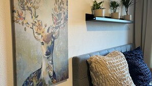 A living room with a painting of a deer, a sofa, a side table, and a shelf with plants.