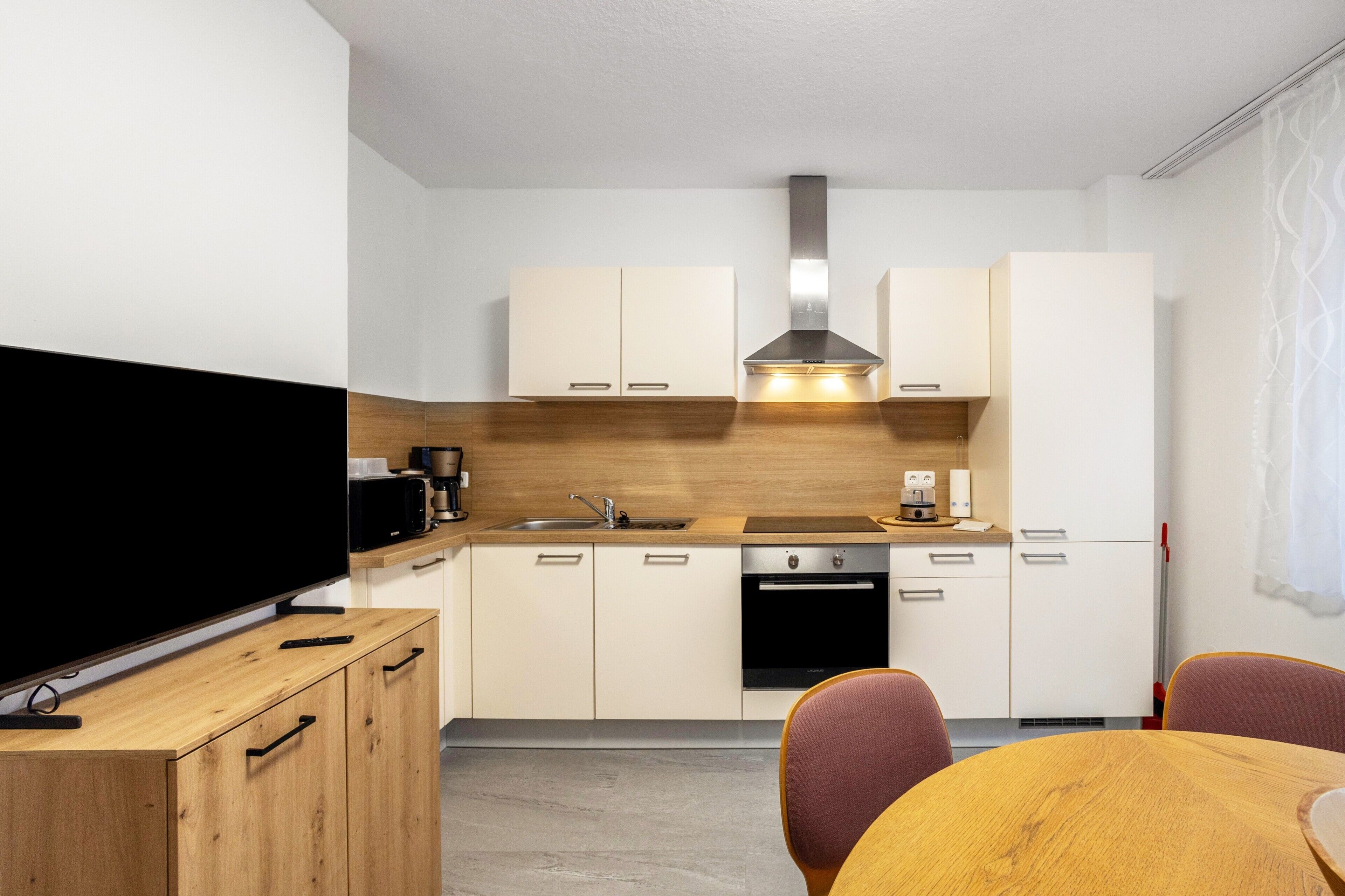 Une cuisine moderne avec des armoires blanches, une hotte de cuisinière en acier inoxydable, un four à micro-ondes et un lave-vaisselle. On y trouve également une table à manger en bois avec des chaises.