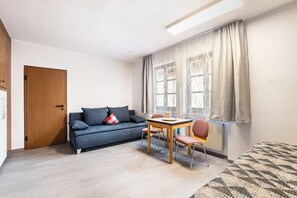 Una habitación con sofá, mesa de comedor con sillas, ventana con cortinas y puerta.