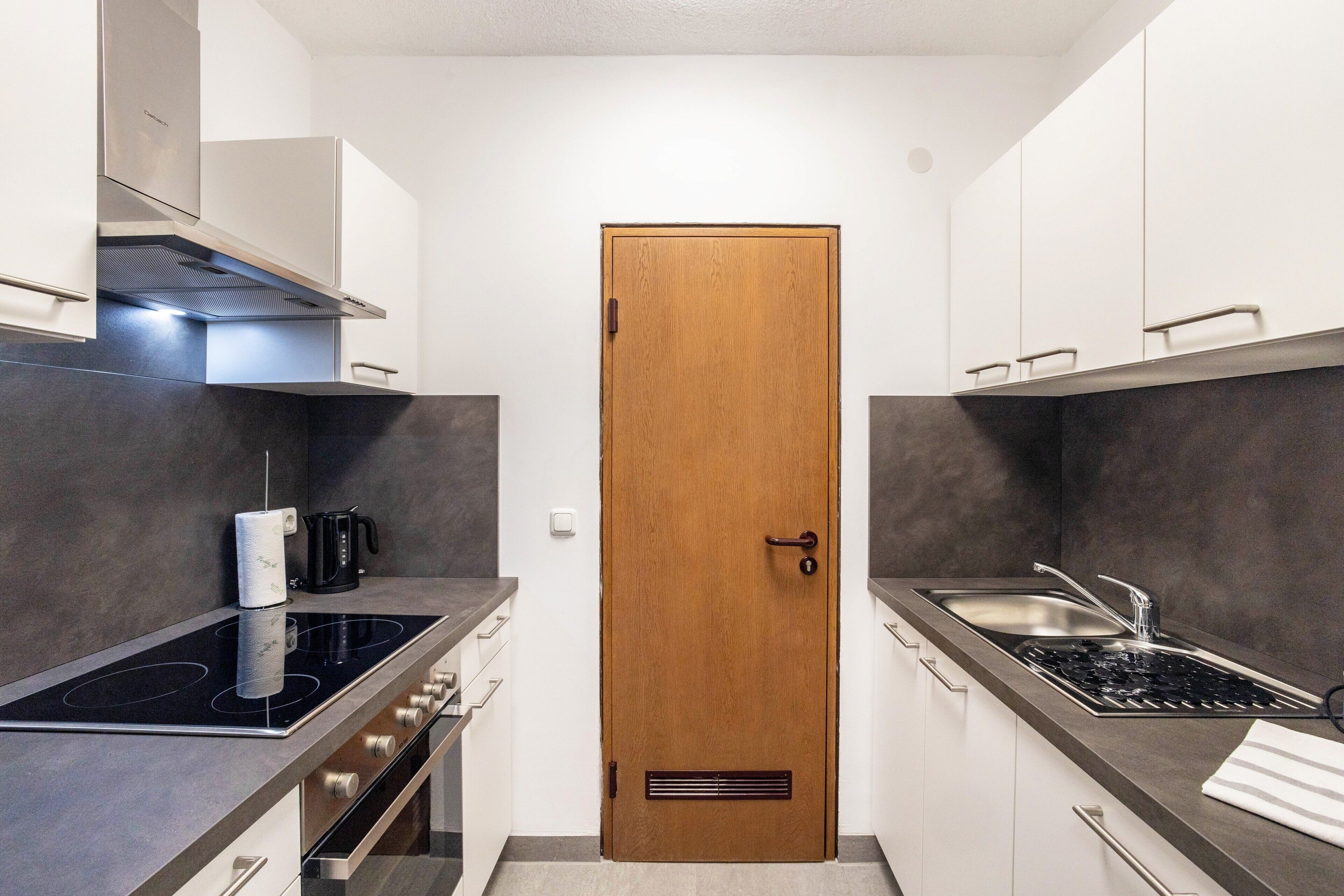 Une cuisine compacte dotée d’une porte en bois, d’appareils électroménagers en acier inoxydable et d’un design moderne.
