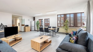 Una sala moderna con un televisor de pantalla plana, una mesa de centro de madera, un sofá gris y una zona de comedor con una mesa y sillas de madera.
