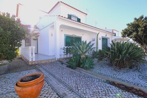 A white building with green shutters, a cobblestone pathway, and a potted plant in the foreground.