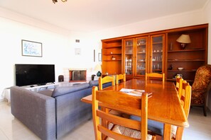A living room with a sofa, TV, wooden dining table, chairs, and a cabinet with glass doors.