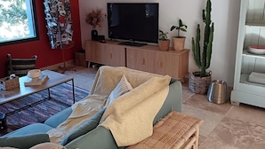 Un soggiorno con un divano verde, una panca in legno, una TV a schermo piatto, un cactus e un tavolino in vimini.