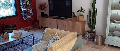 A living room with a green sofa, a wooden bench, a flat-screen TV, a cactus, and a wicker table.