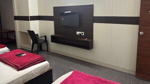 A hotel room with a bed, a chair, a TV mounted on the wall, and a wooden wardrobe. - Aditya Inn (Krishnagiri)