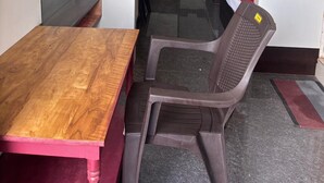 A hotel room with a wooden table, a plastic chair, a bed with a red and white bedspread, and a door marked with the number 201. - Aditya Inn (Krishnagiri)