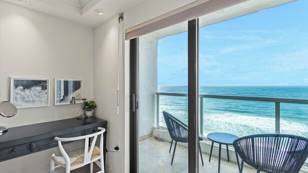 Un balcon avec vue sur l’océan, un bureau avec une chaise et deux fauteuils.