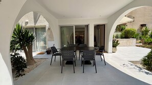 A covered patio with a dining table and chairs, surrounded by white walls and arches. - Kantara Apartment w Pool by TrulyCyprus (Limassol)