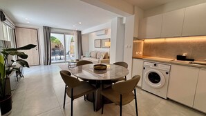 A modern kitchen with a built-in washing machine, a dining area with a round table and chairs, and a view of the outdoors through a glass door. - Kantara Apartment w Pool by TrulyCyprus (Limassol)