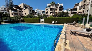 A swimming pool with clear blue water, surrounded by a tiled deck and lounge chairs. - Kantara Apartment w Pool by TrulyCyprus (Limassol)