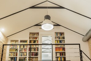 Eine Bibliothek mit Bücherregalen, einer zentralen Leuchte und einer geneigten Decke.
